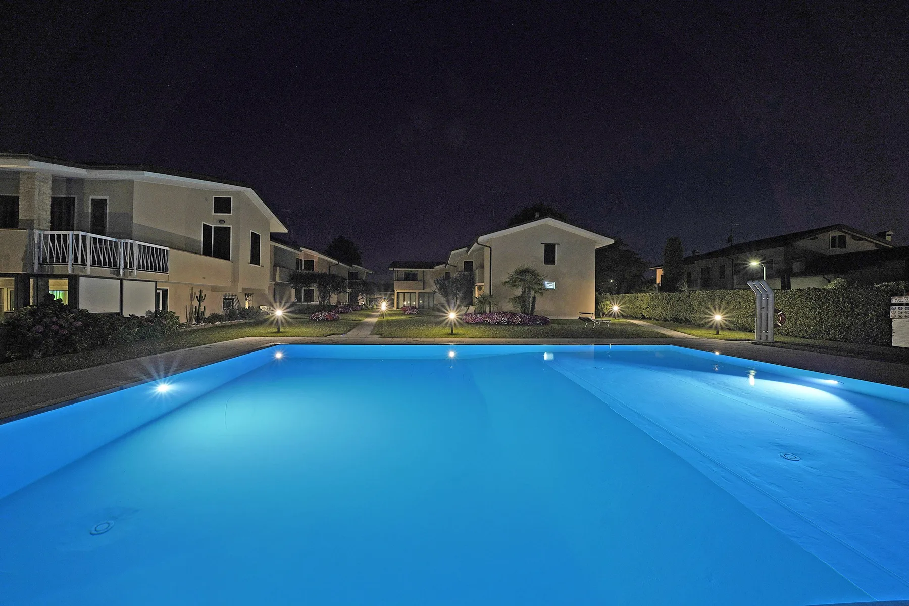 Una piscina brilla en azul por la noche, rodeada de edificios residenciales.