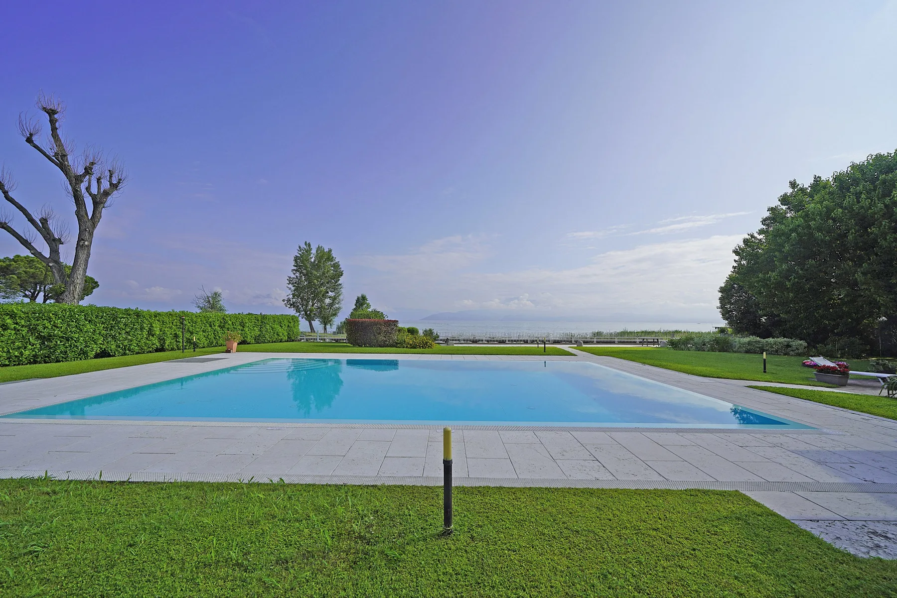 Una piscina al aire libre está junto a un césped, con una vista lejana del agua.