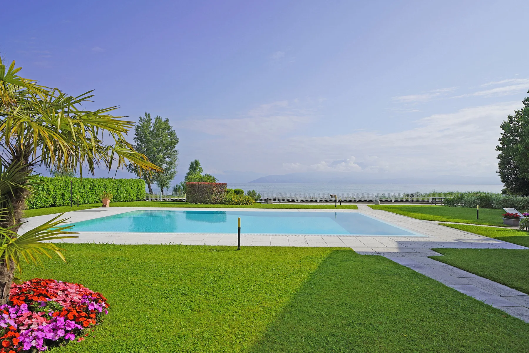 Una piscina está junto a un césped verde, con agua visible a lo lejos.