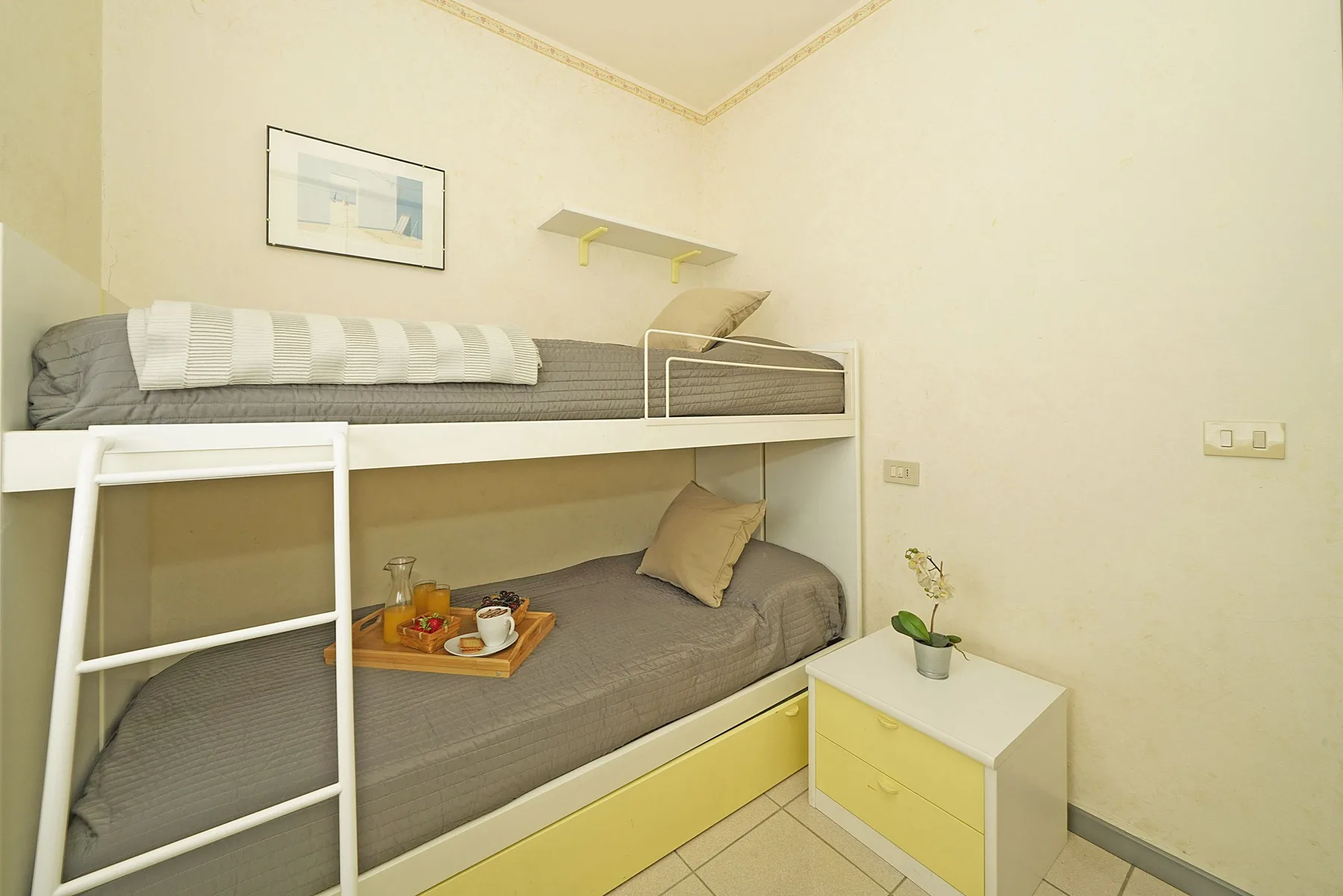 Zona de descanso con una litera, ropa de cama gris y una mesita de noche.