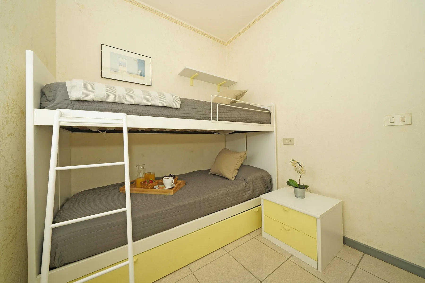 Una zona compacta para dormir con literas, ropa de cama gris y una mesita.