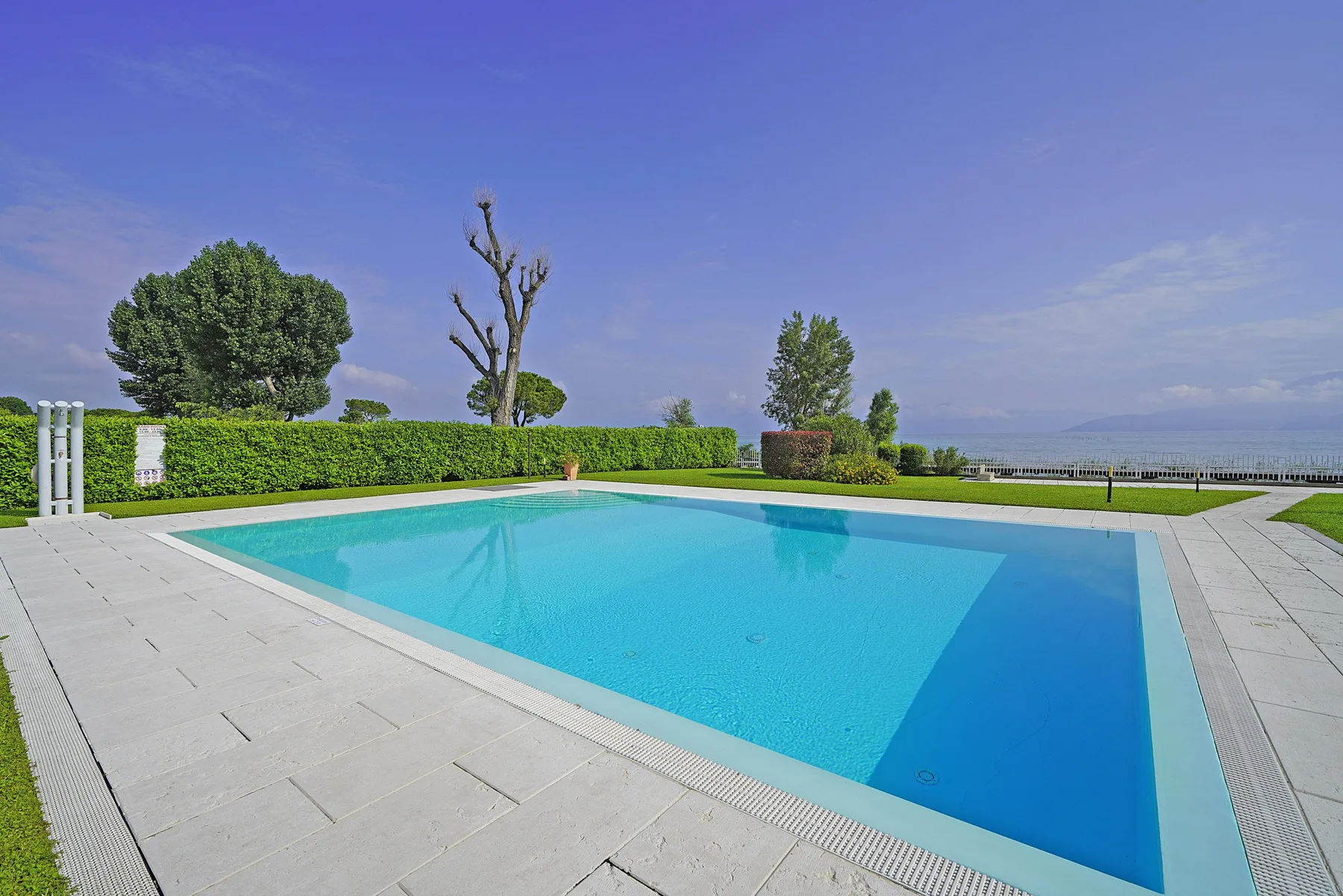 Una piscina al aire libre con pavimento y setos recortados.