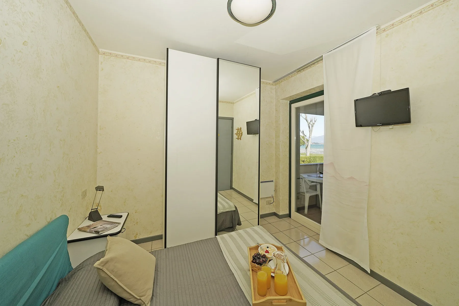 Un dormitorio con una cama, un armario con espejo y un televisor en la pared.