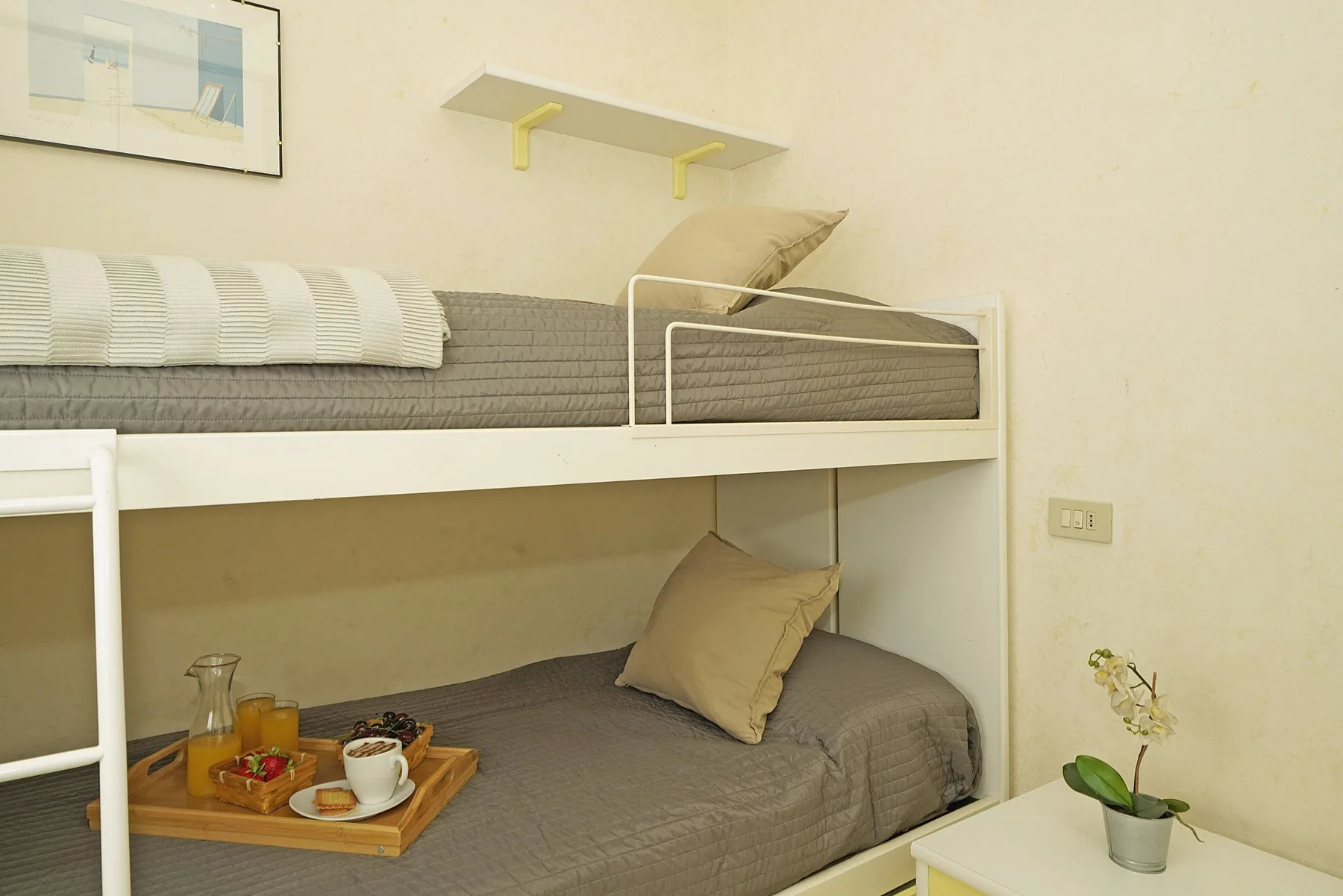 Zona de descanso con una litera, ropa de cama gris y una bandeja en la cama inferior.
