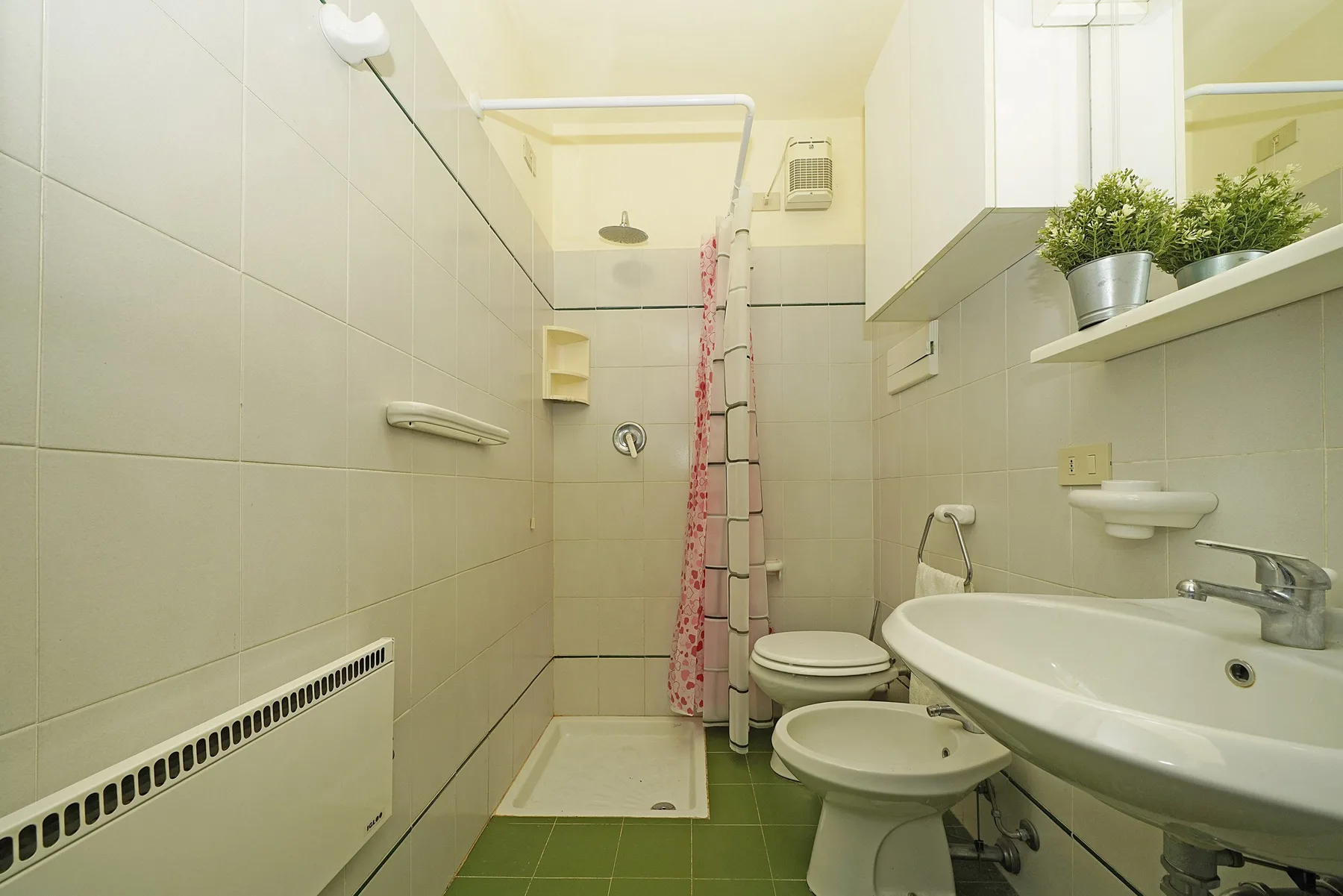 Un baño con azulejos, ducha, inodoro, bidé y lavabo.