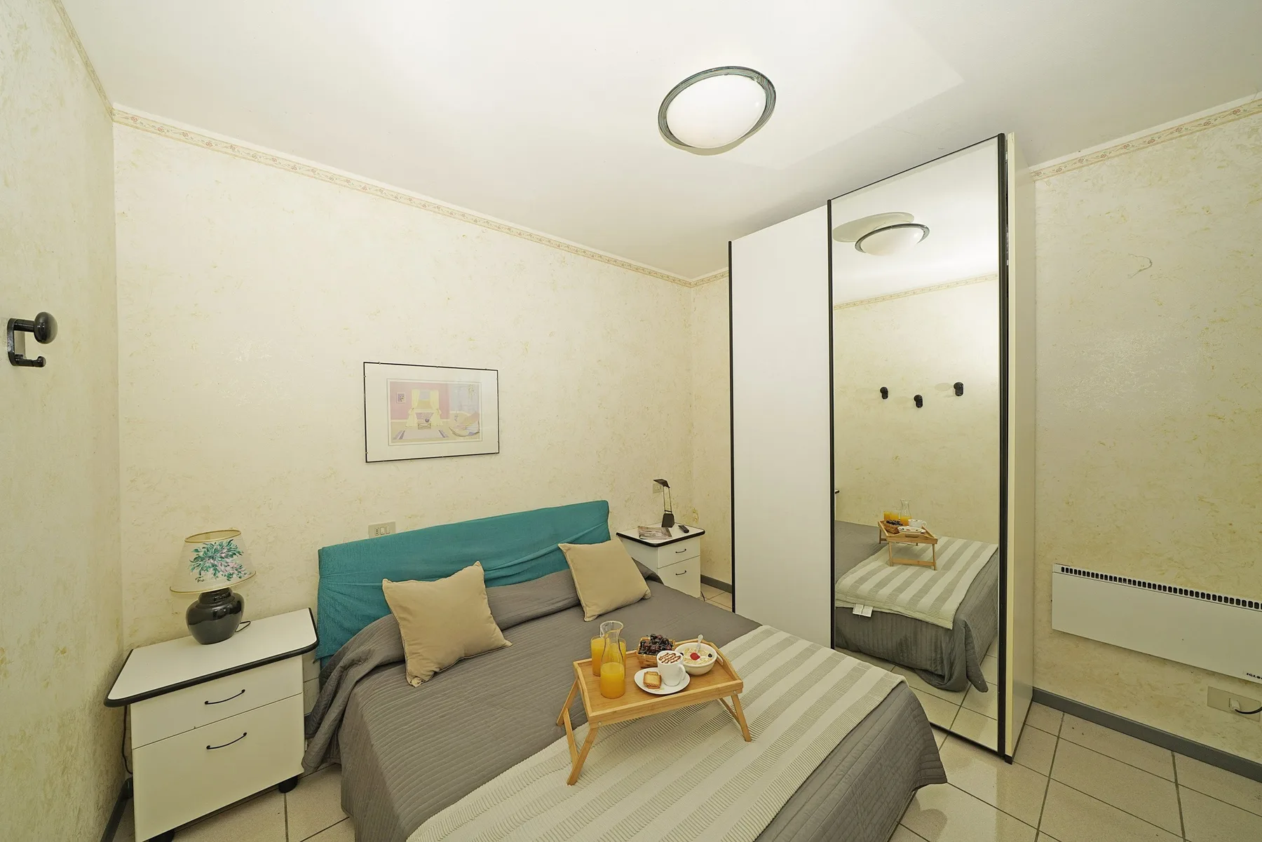 Un dormitorio con una cama, mesitas de noche y un armario con espejo.