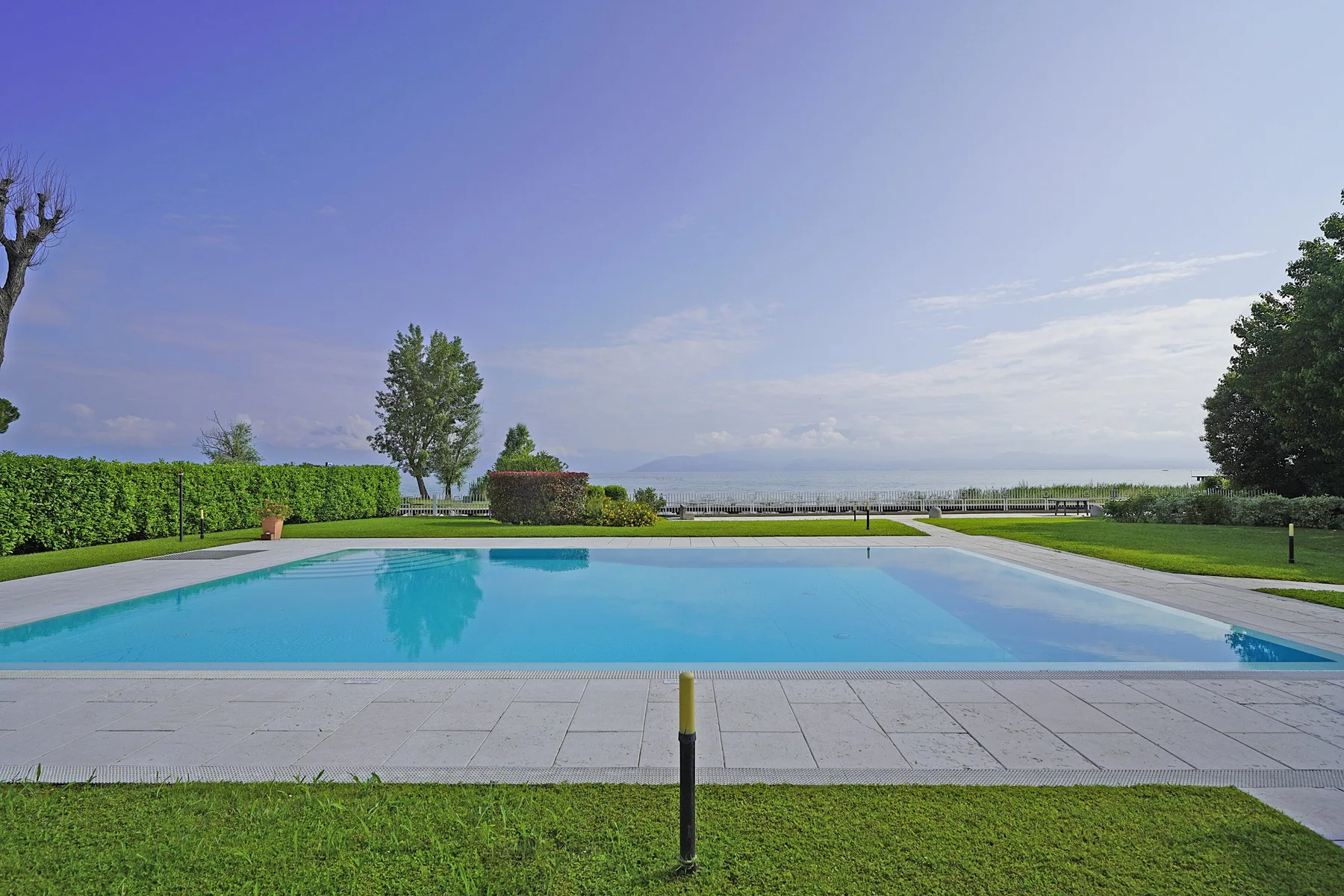 Una piscina al aire libre está junto a una terraza pavimentada y un césped verde.
