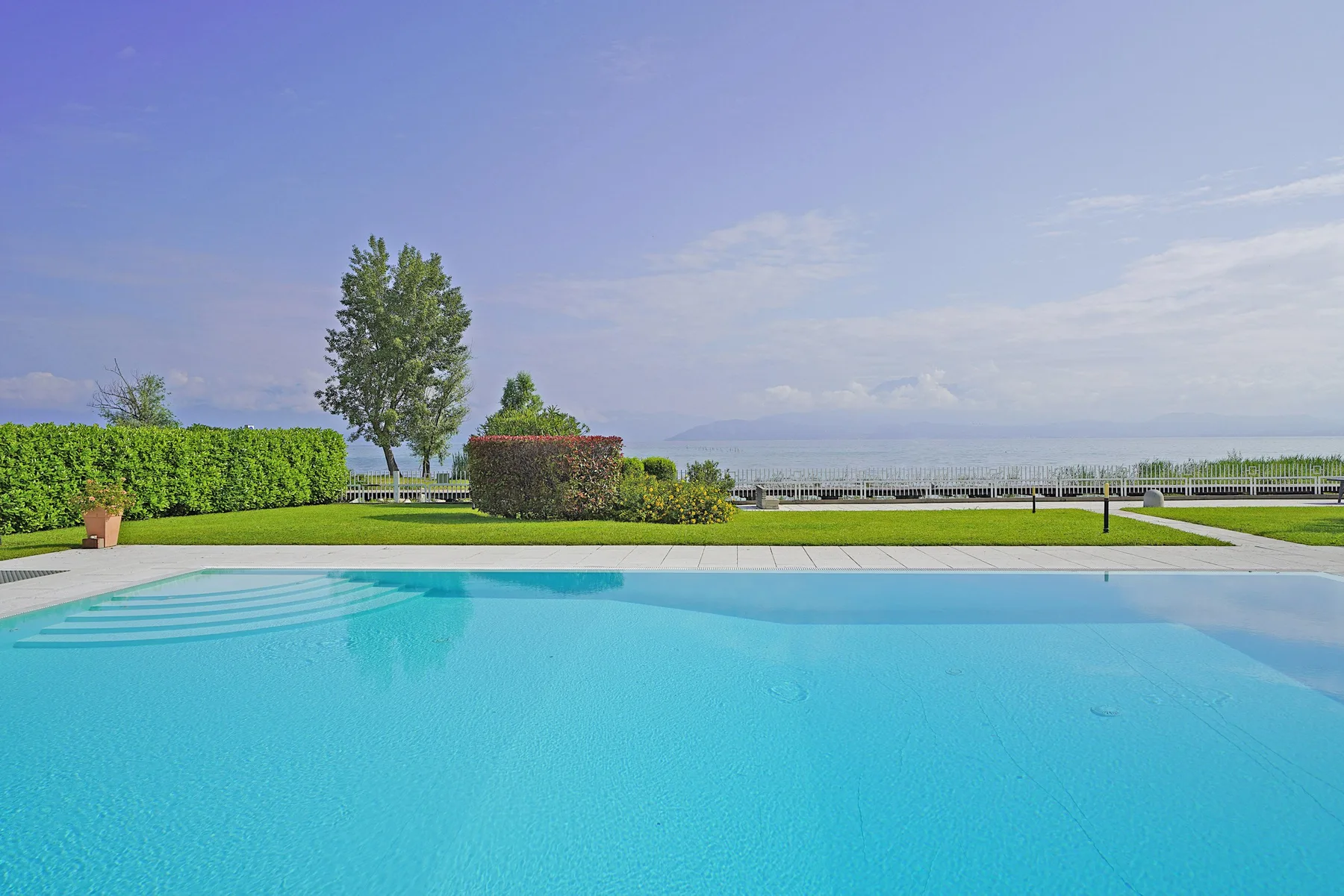 Piscina al aire libre junto a un césped, setos recortados y árboles.