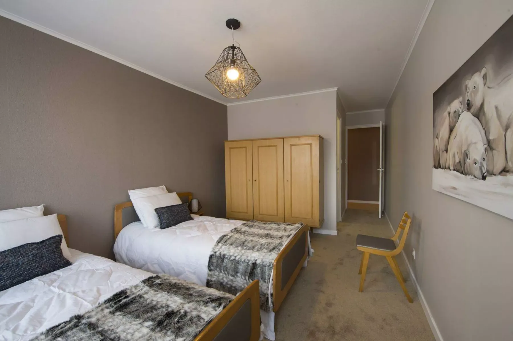 A bedroom with two beds, a wardrobe, and a chair.