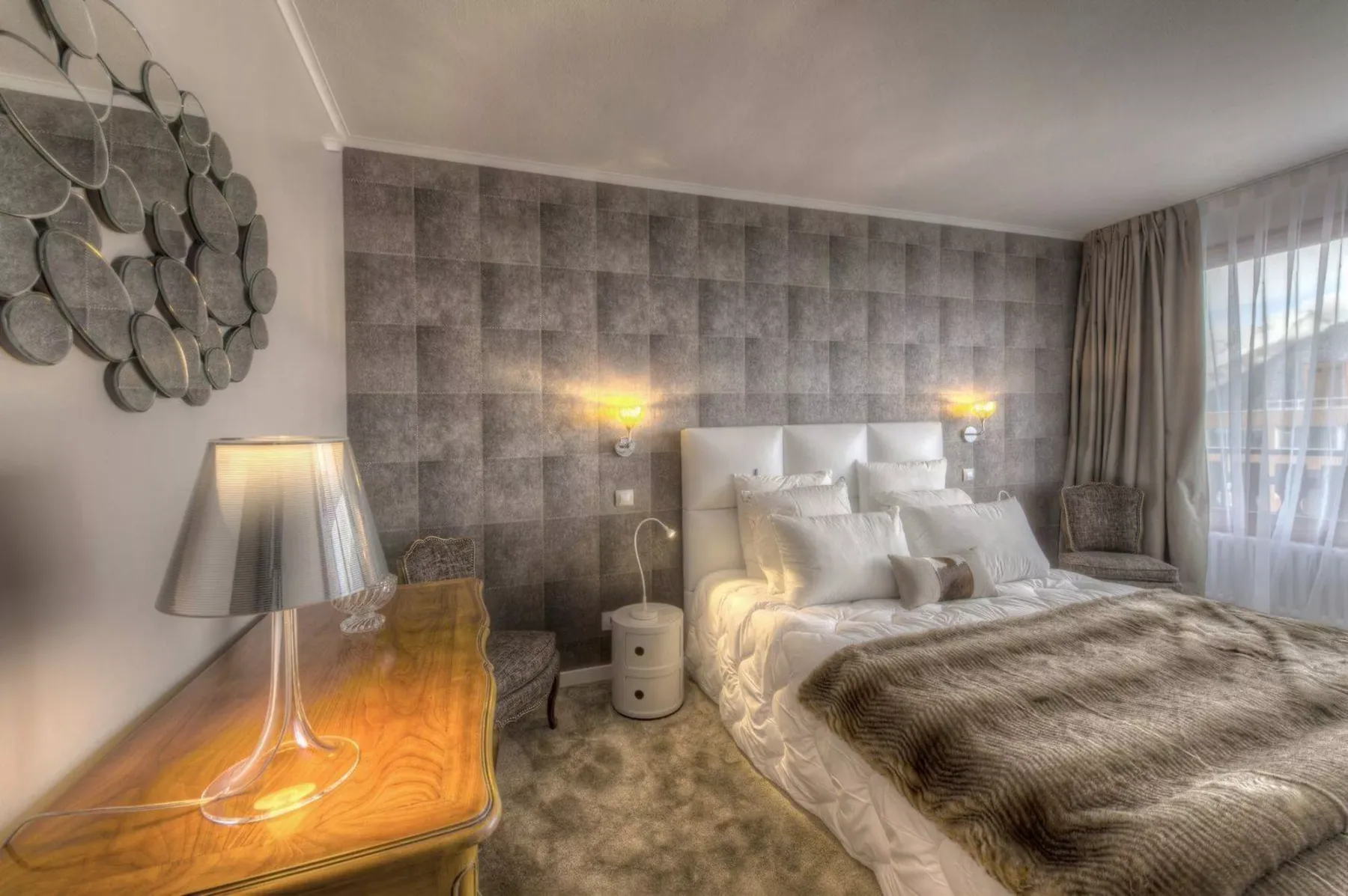 A bedroom with a bed, bedside lights, and a large window.
