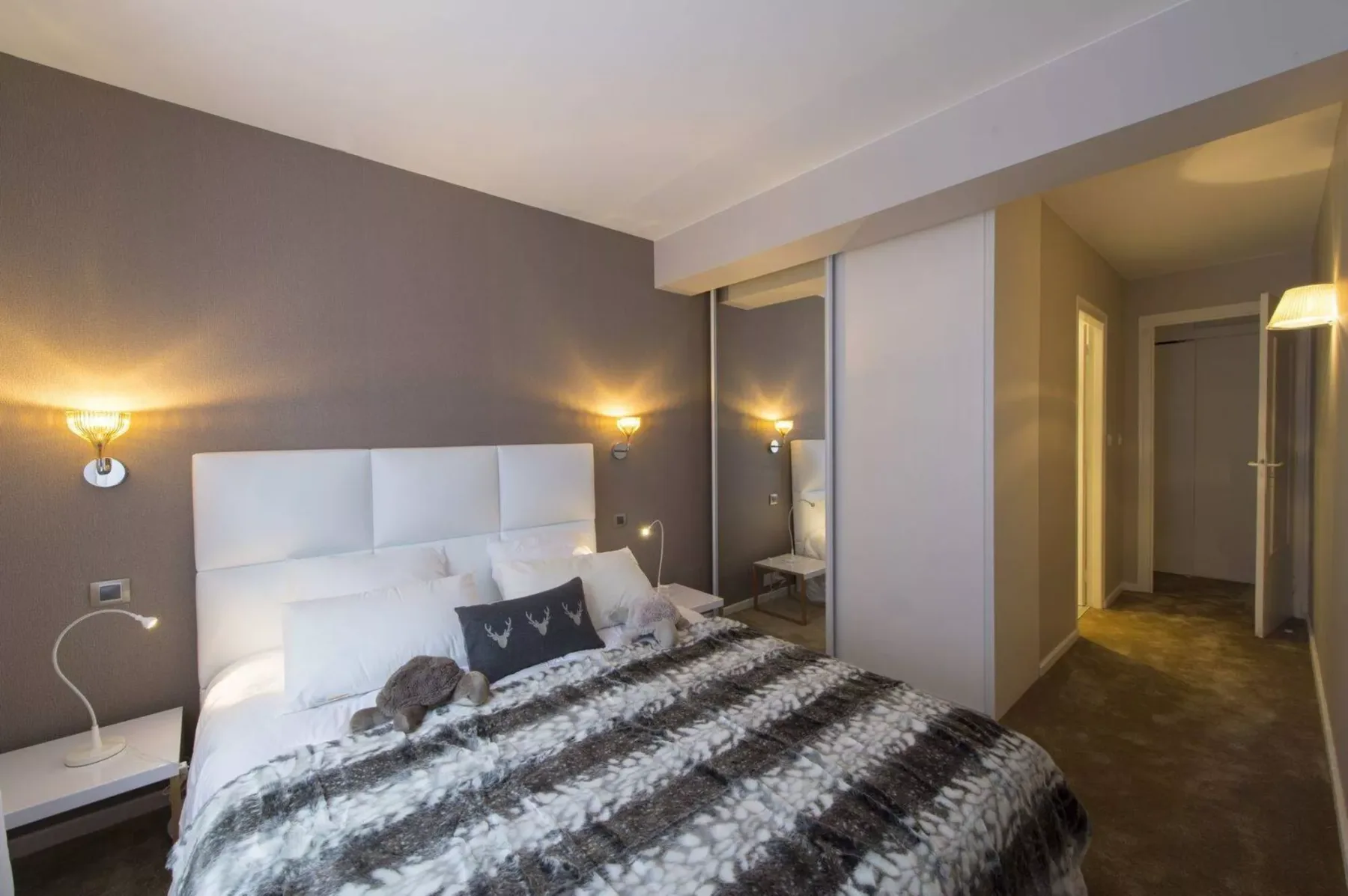 A bedroom with a bed, bedside tables, and a mirrored wardrobe.