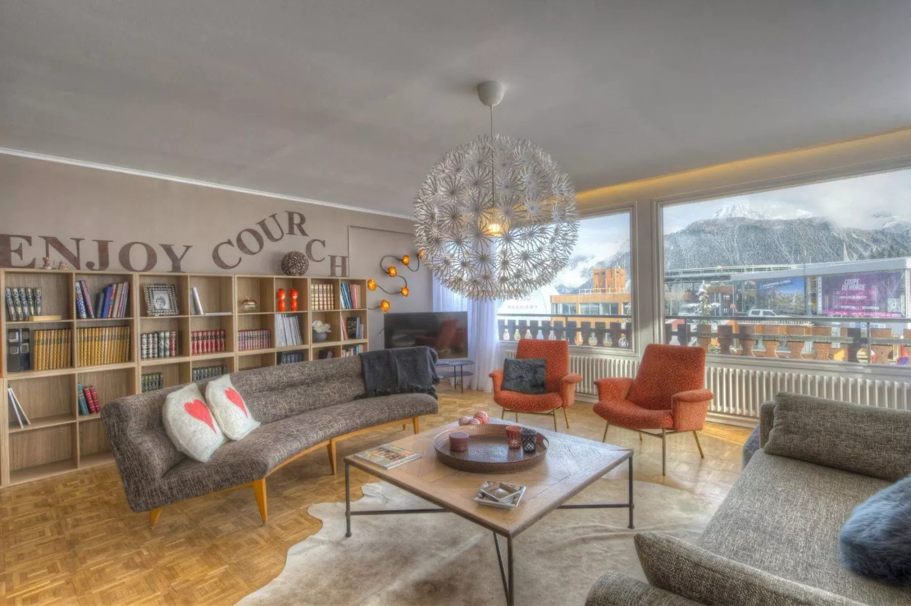 A living room with seating, bookshelves, and large windows.