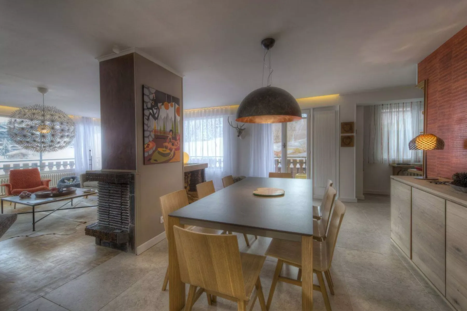 An open-plan dining and living area with a table, seating, and large windows.