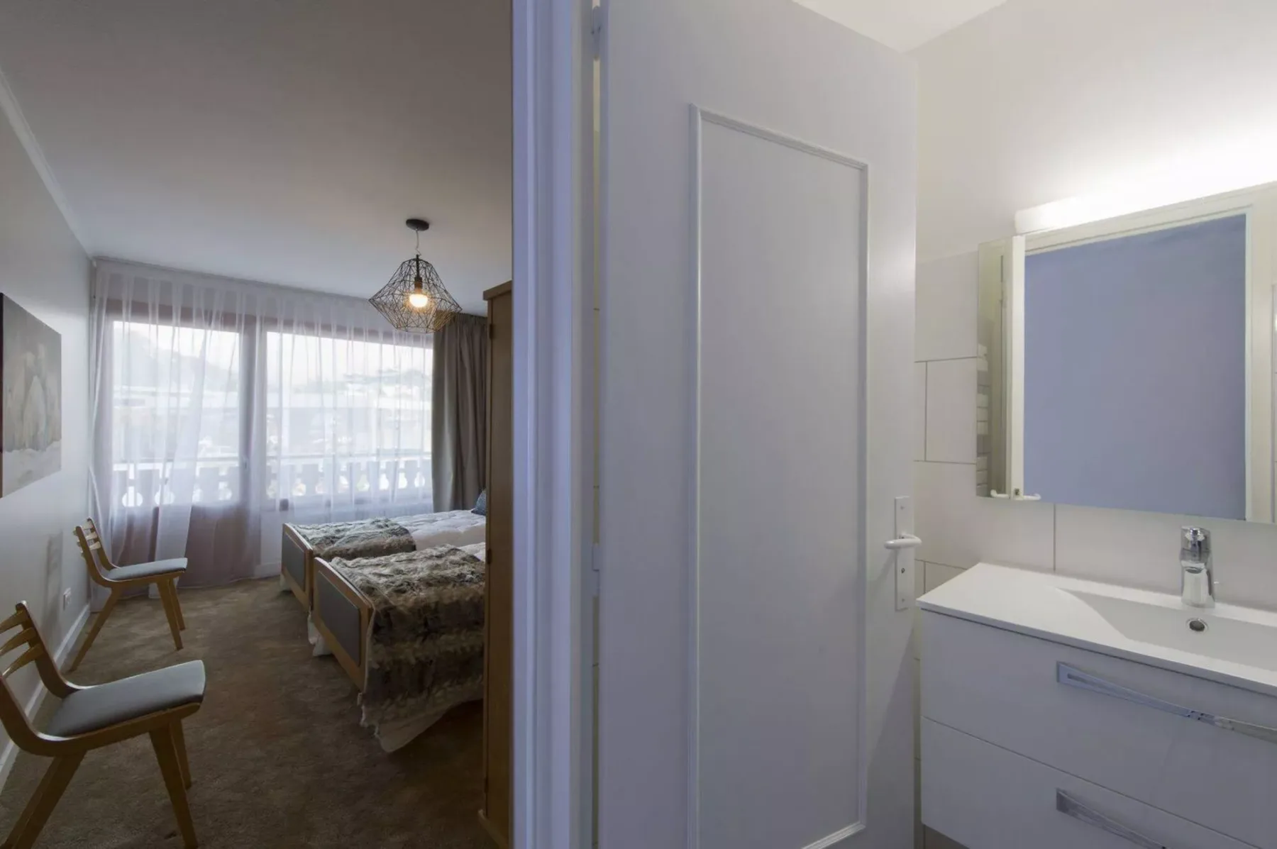 A bedroom with a bed and seating is visible beside a bathroom vanity.