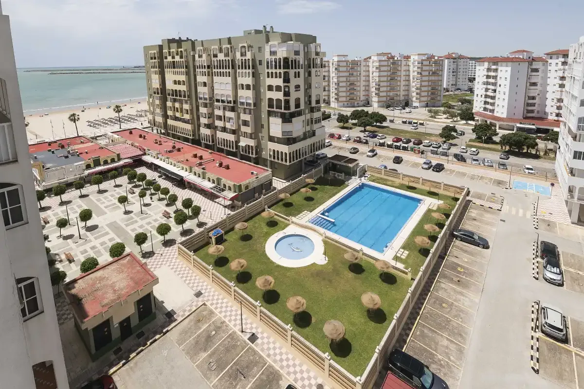 Vista aérea de edificios de apartamentos, una piscina y la playa junto a la costa.