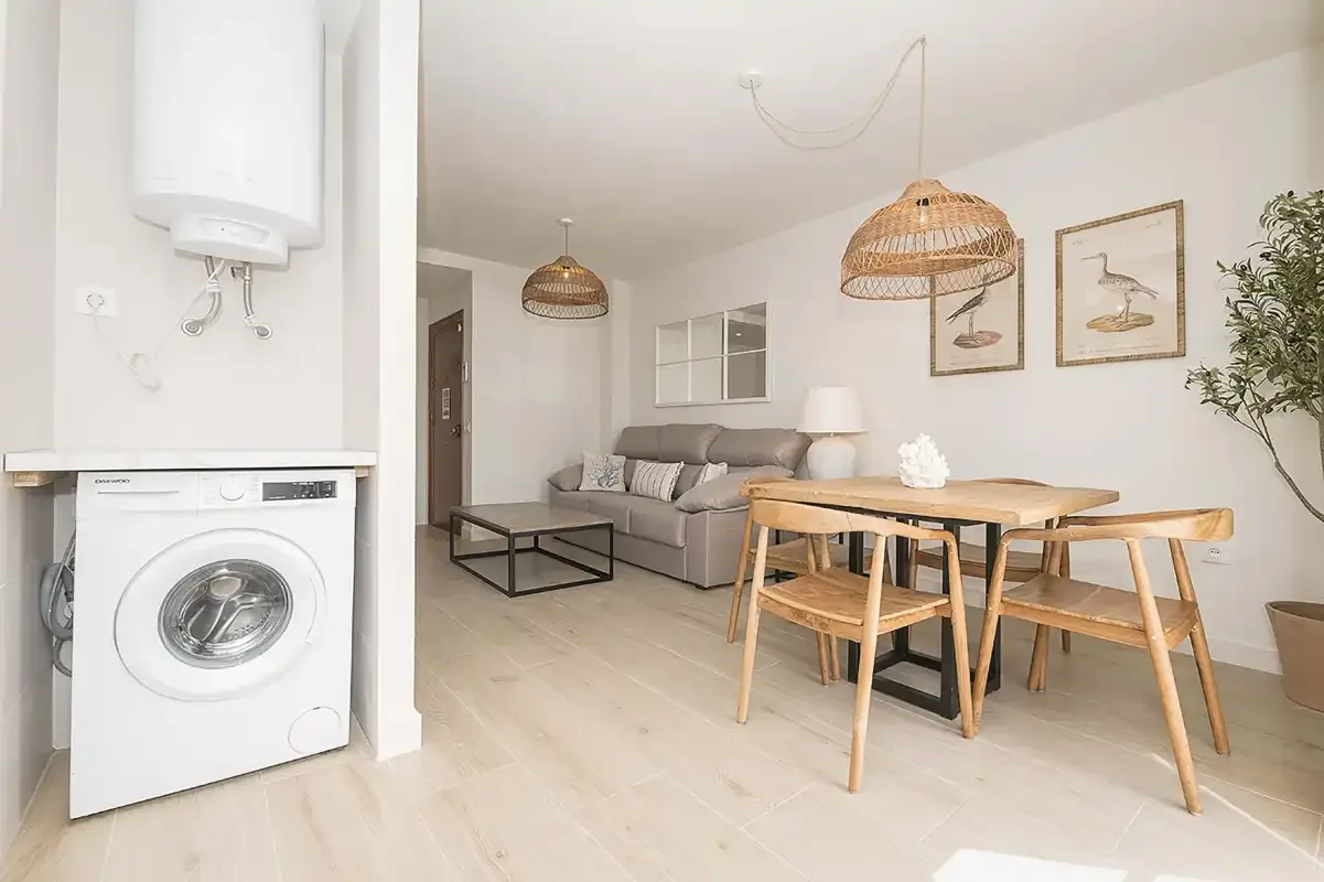 Una luminosa sala de estar y comedor con sofá, mesa de madera y lámparas colgantes de fibras tejidas.