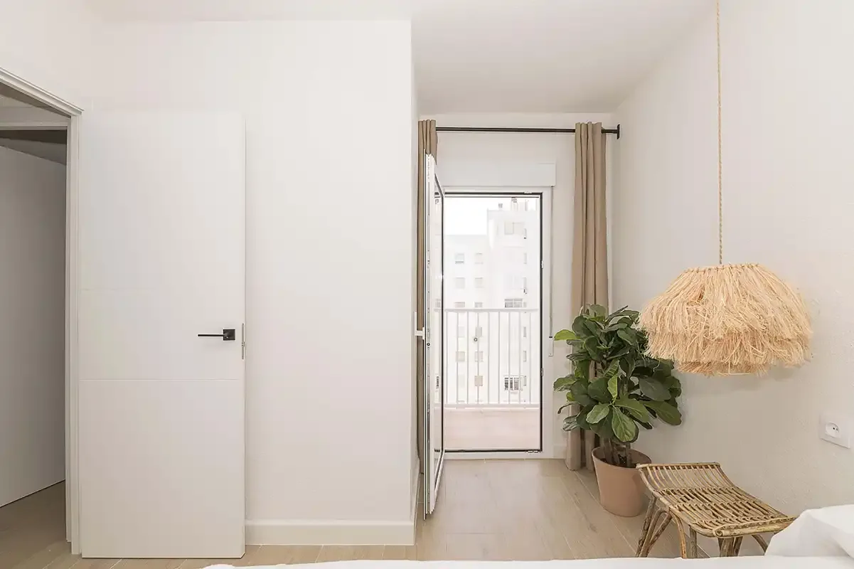 Un dormitorio luminoso con la puerta del balcón abierta y una planta en maceta.
