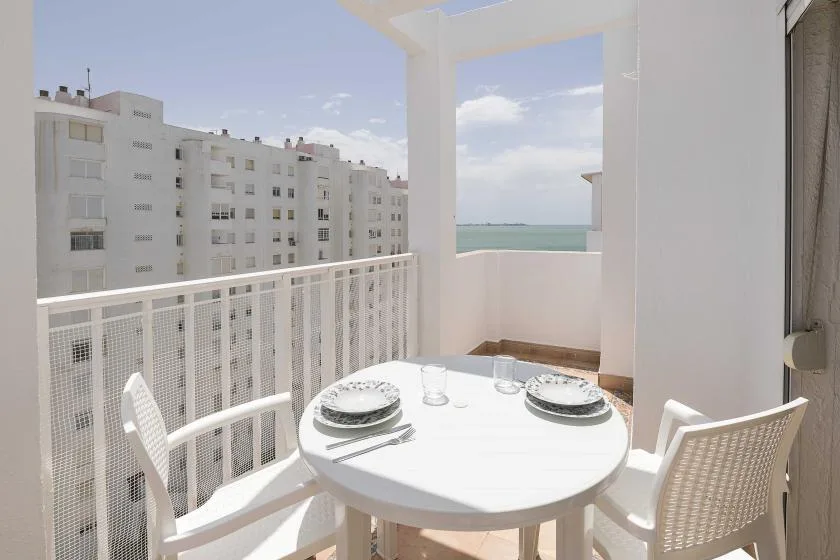 Un balcón soleado con una mesa redonda y asientos con vistas al mar.