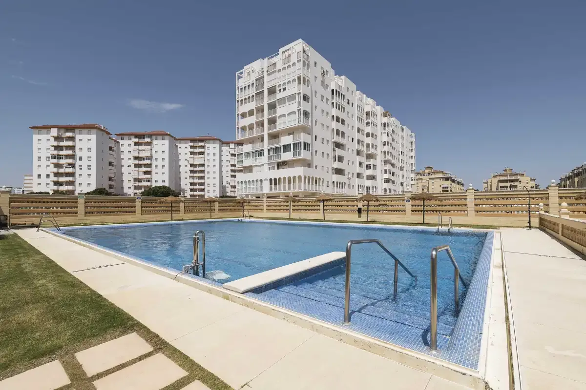Una piscina al aire libre con pasamanos metálicos está frente a varios edificios de apartamentos.