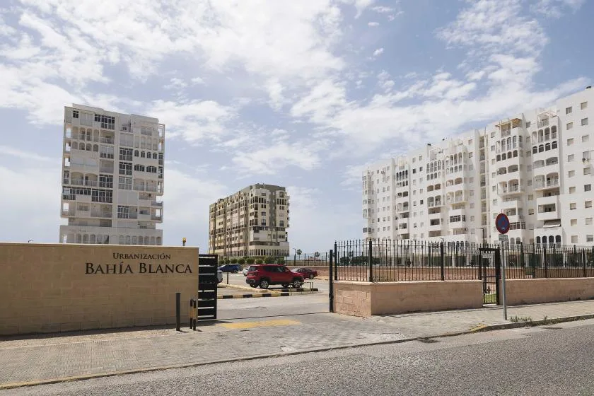 Edificios de apartamentos se alzan tras una entrada con reja junto a una calle pavimentada.