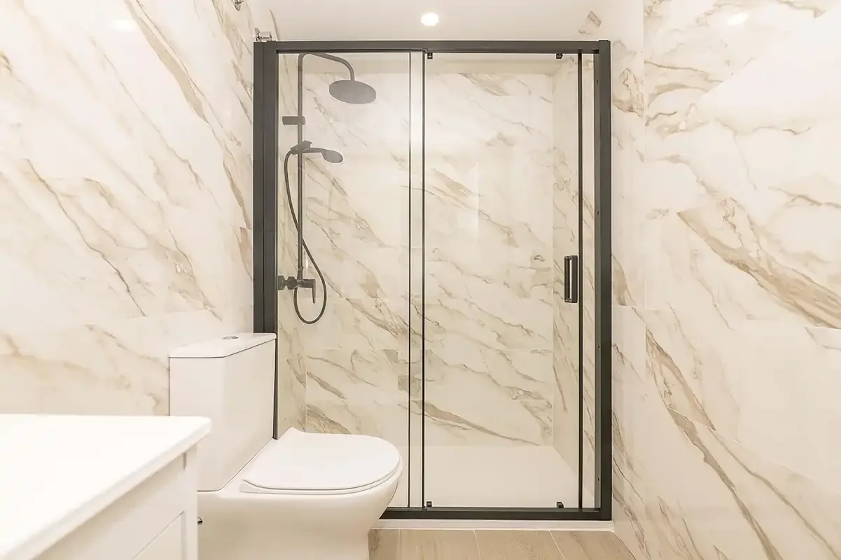 Un baño con ducha de vidrio y paredes claras con vetas.