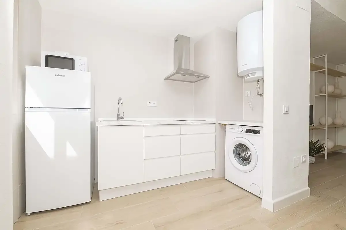 Una pequeña zona de cocina con armarios blancos, un refrigerador y una lavadora.