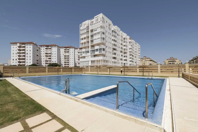 An outdoor swimming pool sits beside apartment buildings under a clear sky.