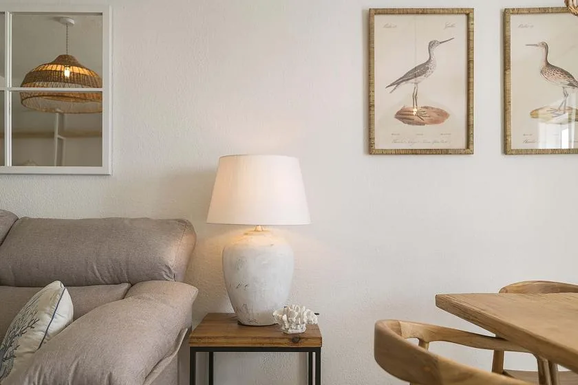 Sala de estar con asientos tapizados, una lámpara de mesa e ilustraciones de aves enmarcadas.