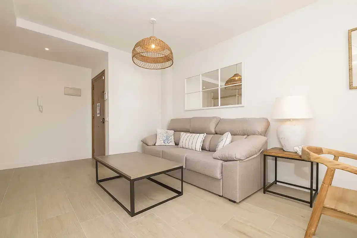 Un salón luminoso con un sofá beige y una mesa de centro baja.