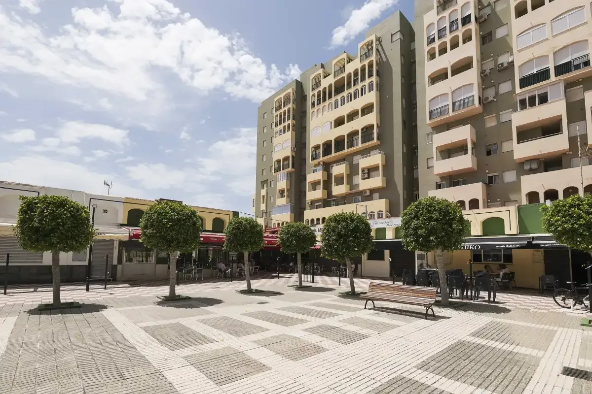 Una plaza pavimentada abierta con árboles y bancos frente a edificios de apartamentos.