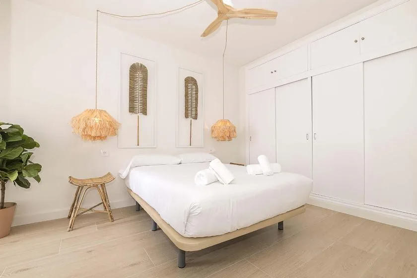 Un dormitorio luminoso con una cama blanca, armarios empotrados y lámparas colgantes.
