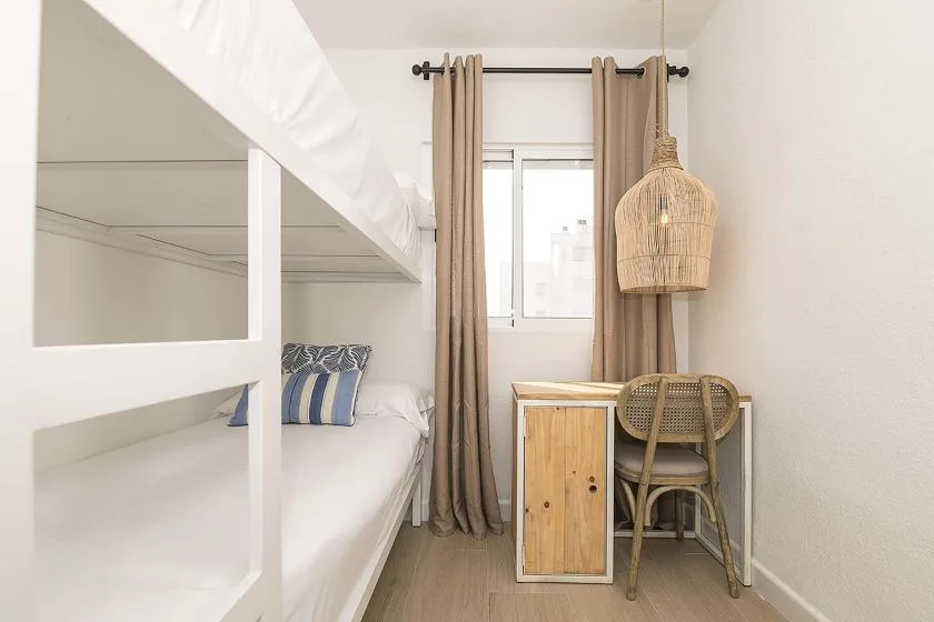 Un dormitorio luminoso con una litera blanca y un pequeño escritorio junto a la ventana.