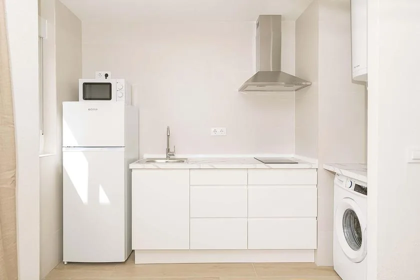 Una cocina luminosa con armarios blancos, un refrigerador y una lavadora.