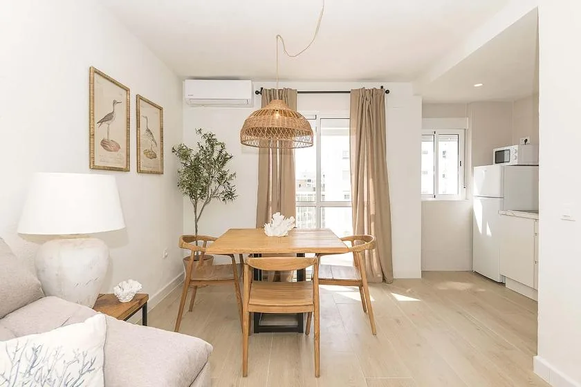 Una luminosa zona de comedor y sala de estar con una mesa de madera junto a la cocina.