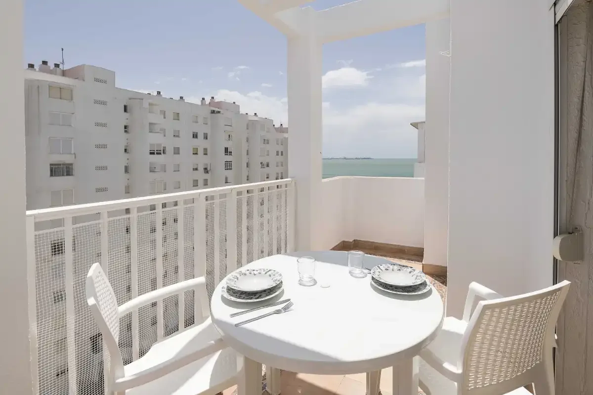 Una luminosa zona de comedor en el balcón da a edificios cercanos y una franja de mar.