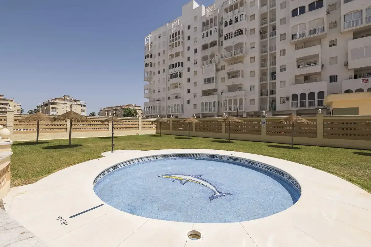 Una piscina circular está en un patio ajardinado rodeado de edificios de apartamentos.