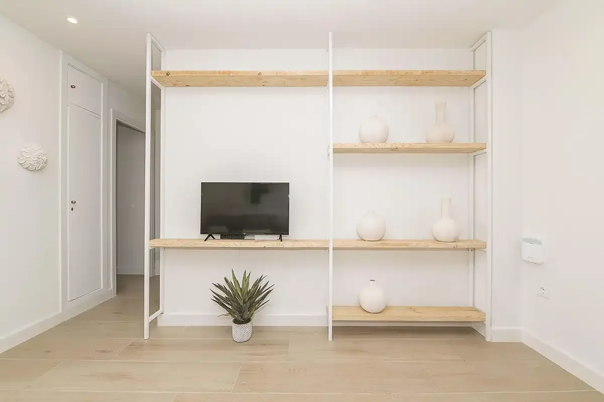 Un salón luminoso con un televisor y estanterías abiertas.