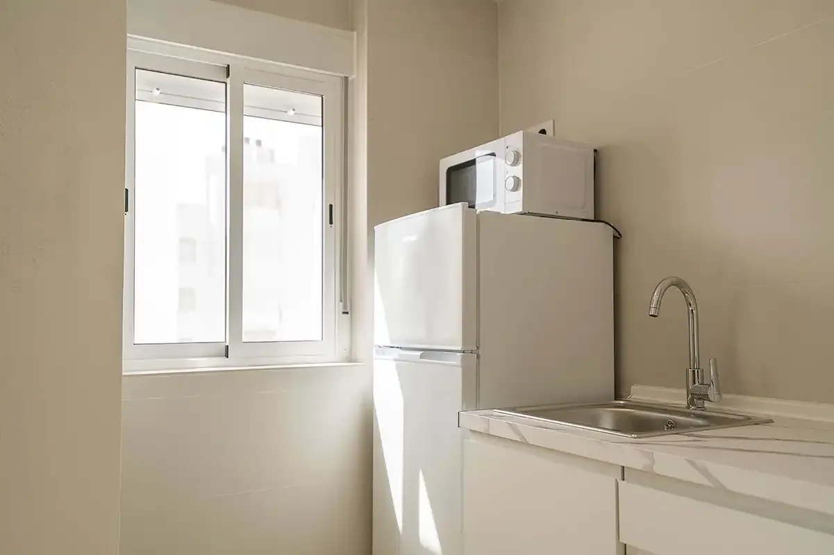 Una cocina compacta con refrigerador, microondas y fregadero junto a una ventana.
