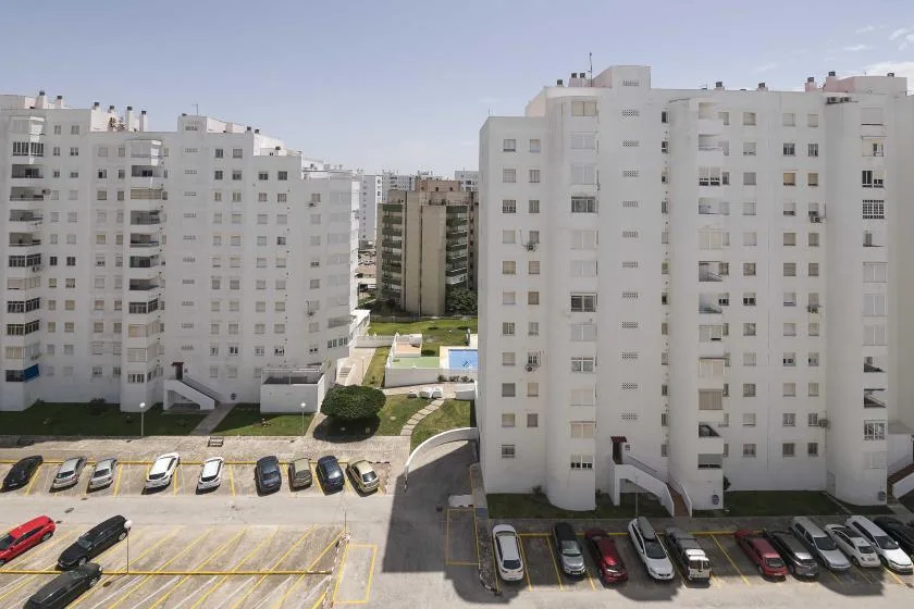 Edificios de apartamentos rodean un área de estacionamiento con espacios señalados y autos estacionados.