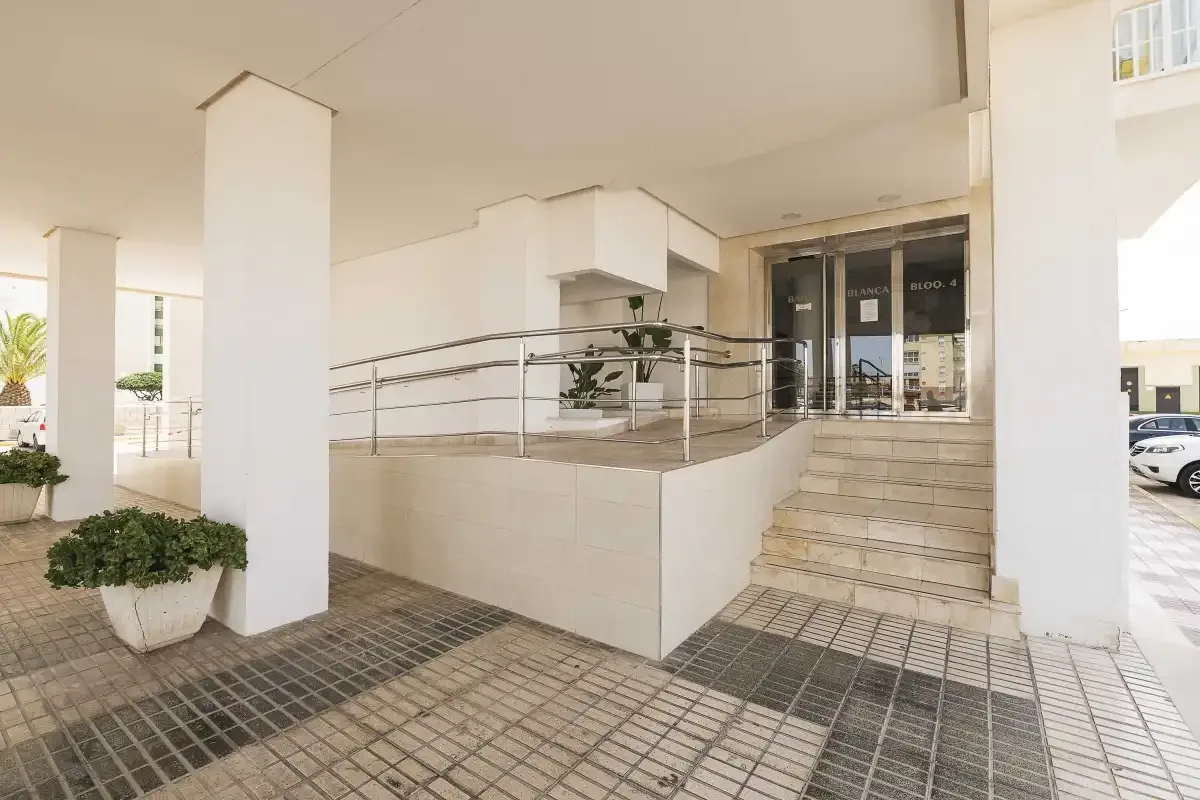 Una entrada cubierta tiene pavimento de baldosas, escalones y barandillas metálicas.
