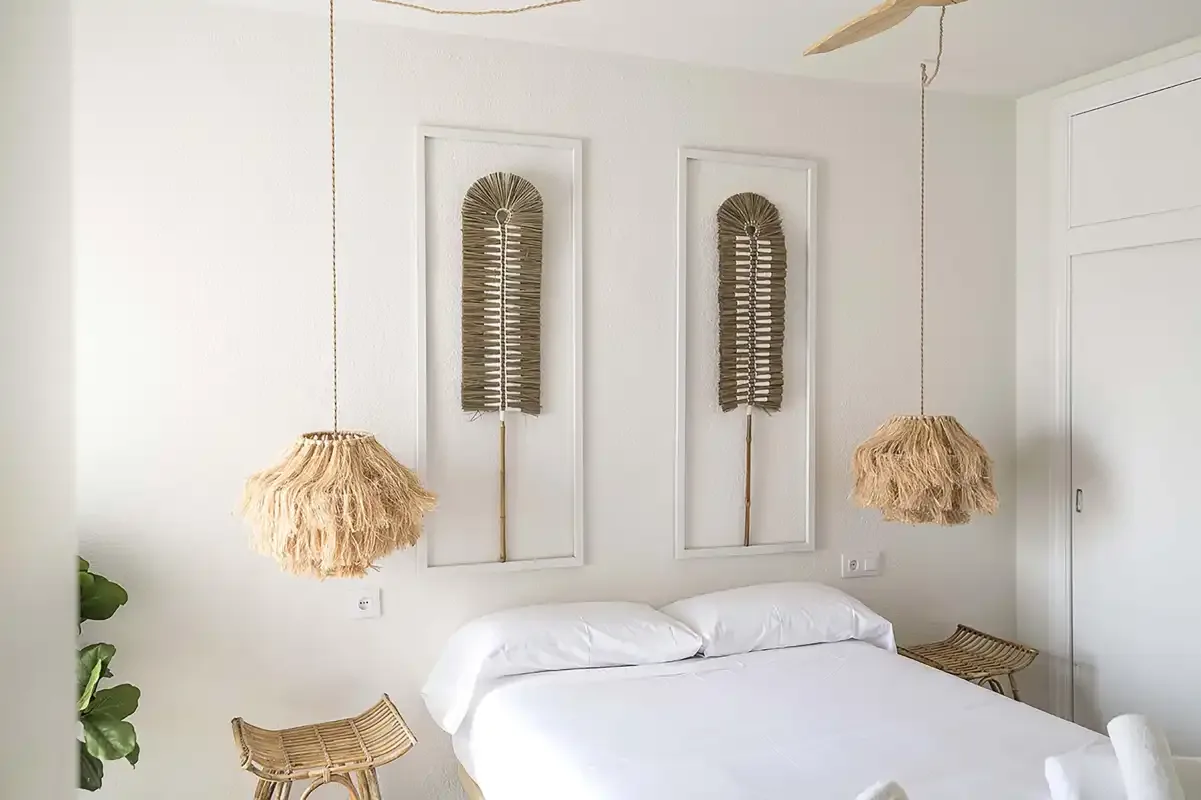 Un dormitorio luminoso con una cama blanca y lámparas colgantes tejidas.