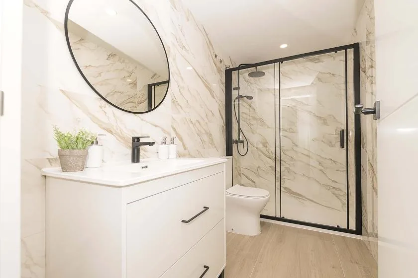 Un baño luminoso con tocador, espejo redondo y ducha de vidrio.
