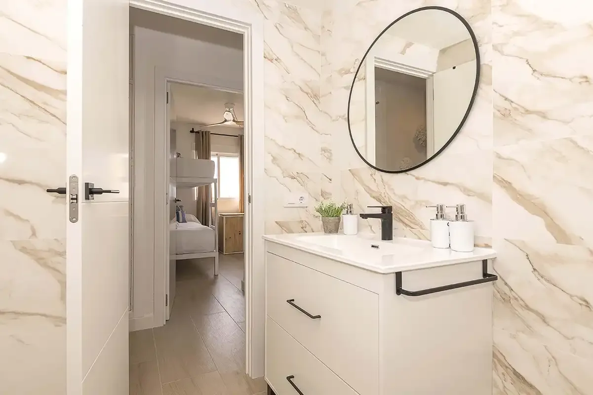 Un tocador de baño con un espejo redondo y una puerta abierta.