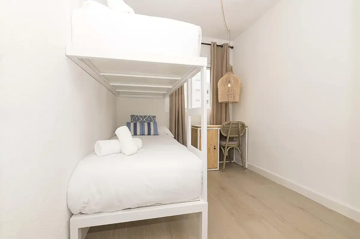 Un dormitorio luminoso con literas, un pequeño escritorio y suelo de madera clara.