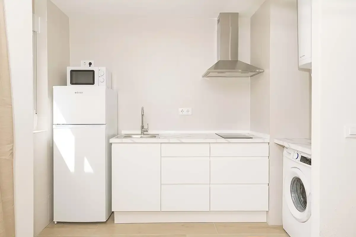 Una cocina luminosa y compacta con armarios blancos y una lavadora.