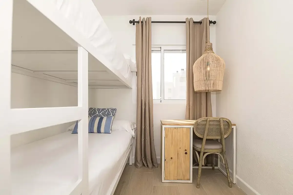 Un dormitorio luminoso con literas, una ventana y un pequeño escritorio.