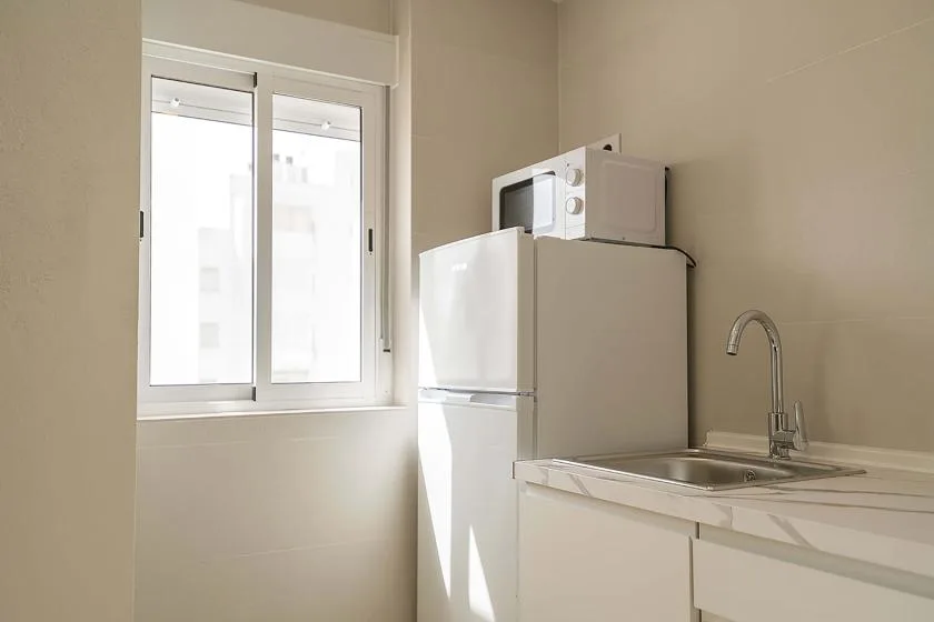 Una cocina pequeña con refrigerador, microondas, fregadero y una ventana luminosa.