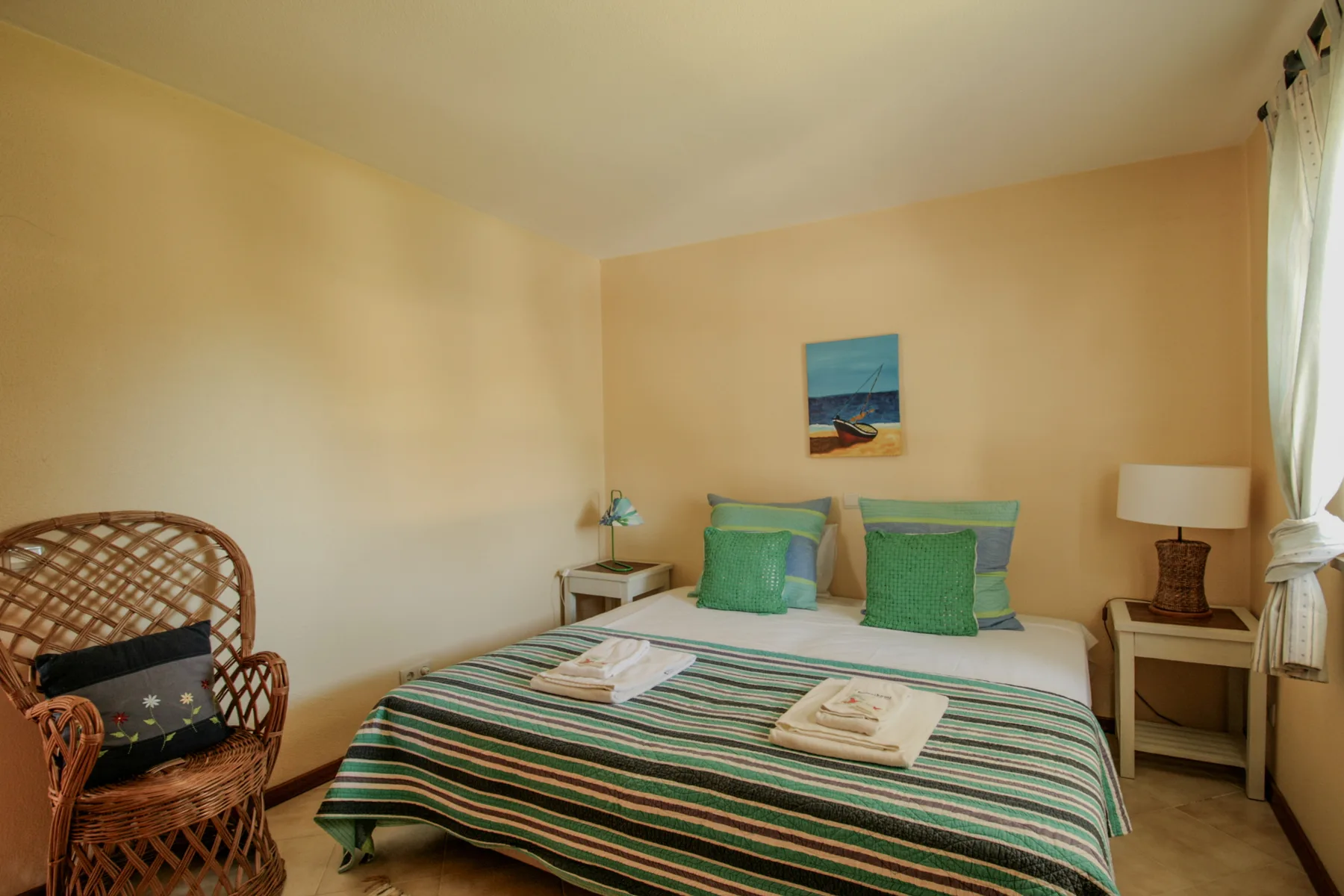 Un dormitorio con una colcha a rayas y una silla de mimbre.