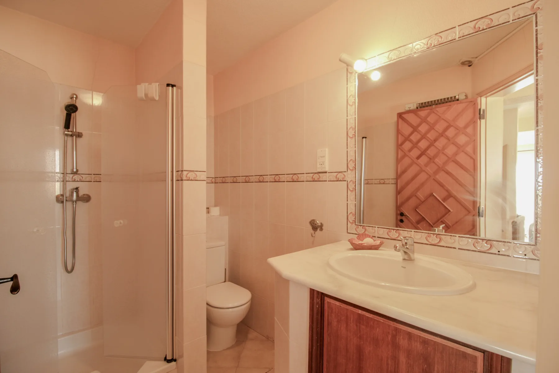 Un baño con ducha, inodoro y lavabo bajo un espejo grande.