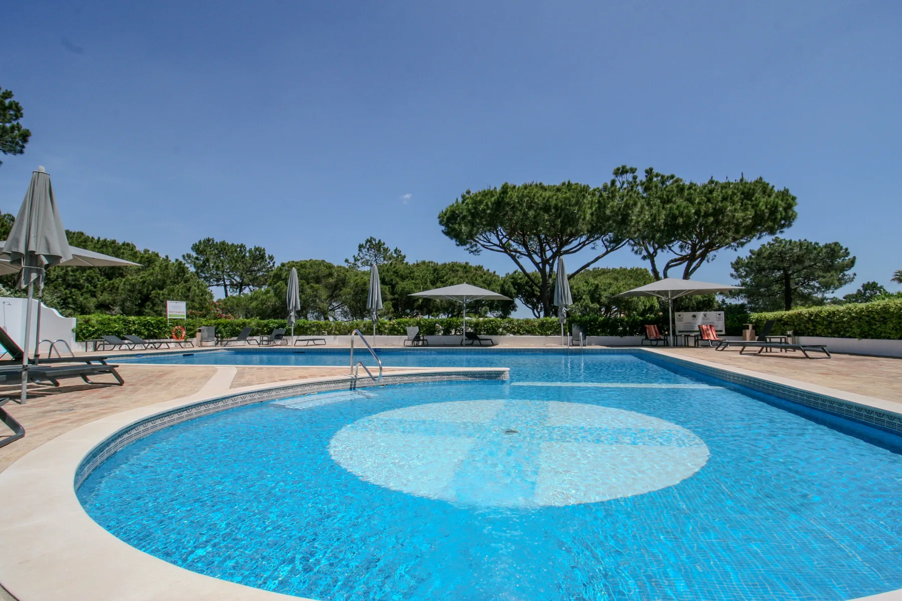 Una piscina al aire libre con una zona circular poco profunda y tumbonas.